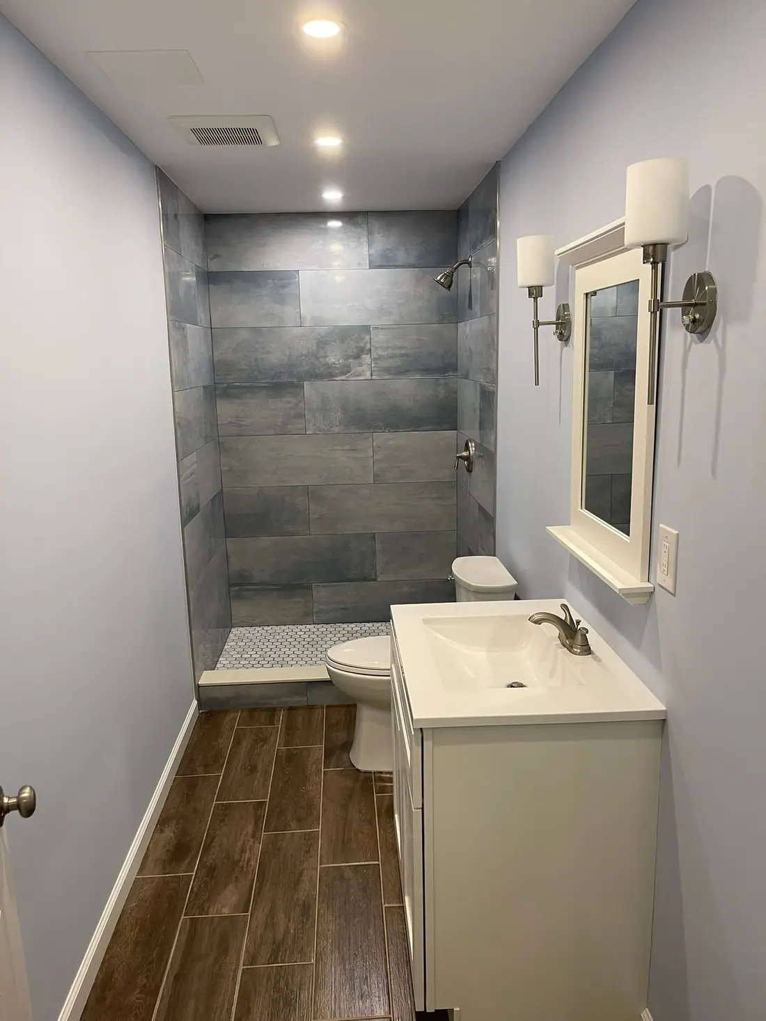 Remodeled bathroom with a blue-gray tile shower, white vanity and plank flooring